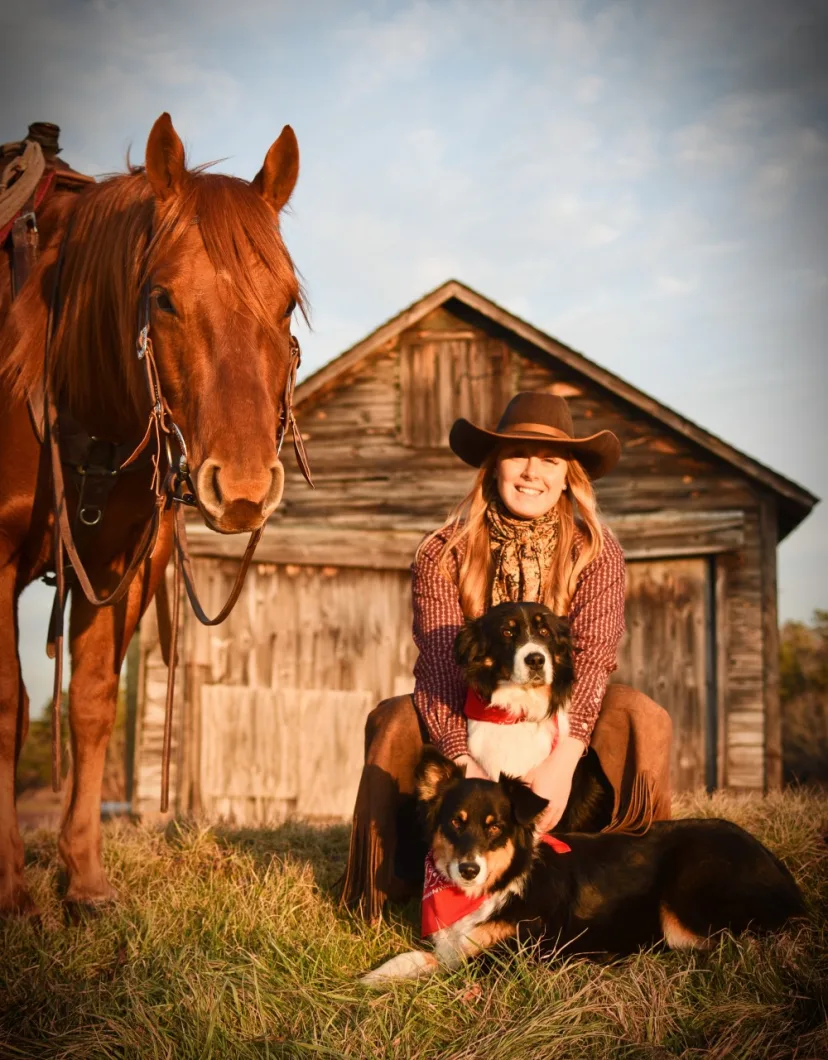 Lisa in front of a barn with herding dogs and a horse